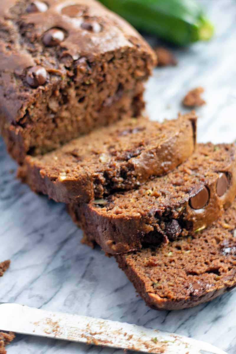 A vertical close up of a loaf of chocolate bread with several sliced pieces lying on a marble countertop.