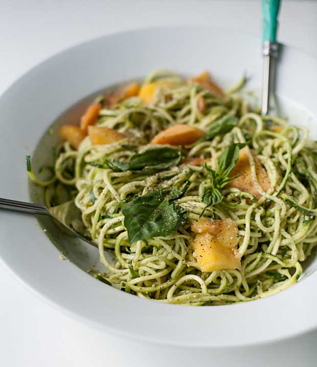 A vertical photo of a bowl of spaghetti with a pesto sauce on a white background.