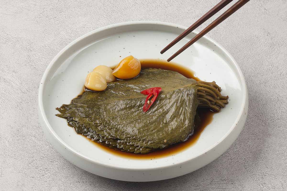 A horizontal image of a white dish with perilla leaves in soy sauce with garlic on the side.