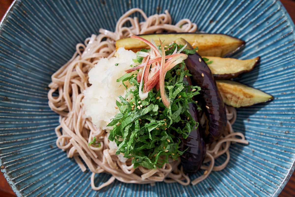 A close up horizontal image of a noodle dish garnished with shiso leaves.