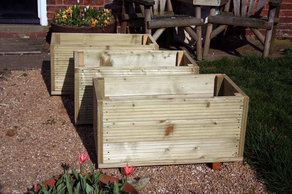 A set of three above-ground planters made from decking timber pictured in bright sunshine.