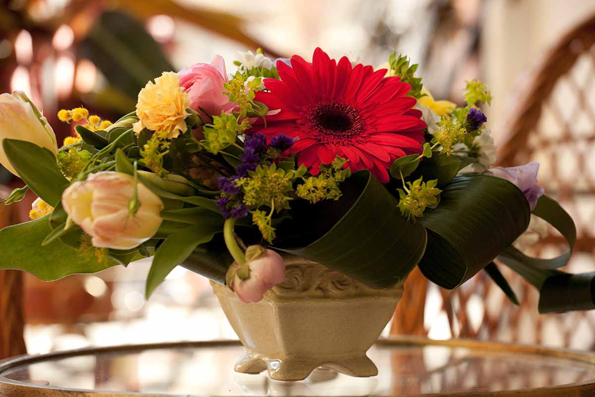 A horizontal image of a bouquet of fresh blooms in a small flat container on a glass table.