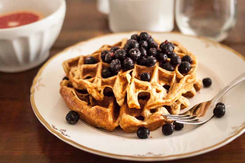 A close up horizontal image of einkorn waffles topped with dark berries.