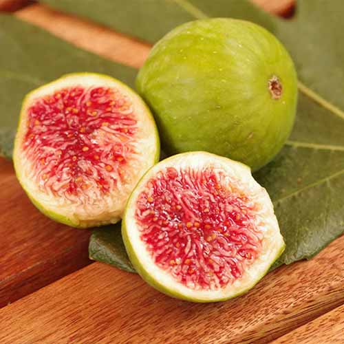 A square image of two 'Desert King' figs one cut in half and the other whole, set on a wooden table.