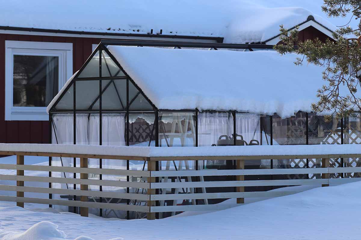 A close up horizontal image of a greenhouse in the garden covered in snow outside a residence.