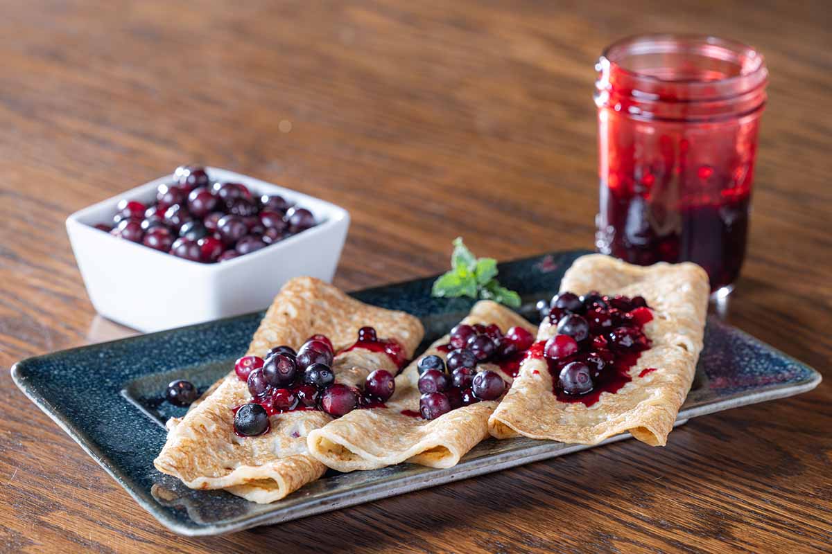A close up horizontal image of pancakes with berry compote set on a wooden surface.