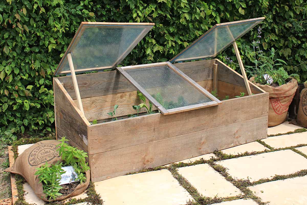 A close up horizontal image of a wooden cold frame on a tiled patio in fall.