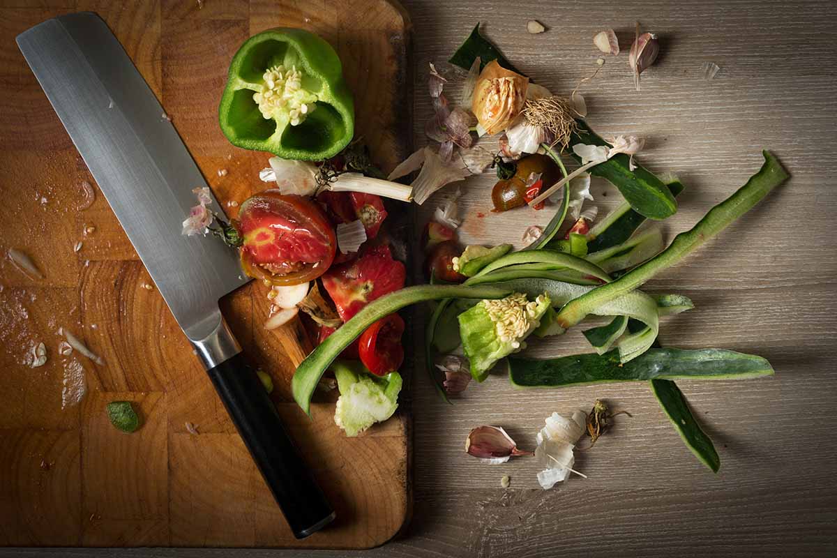 A close up horizontal image of a wooden chopping board and a knife with kitchen scraps ready to place on the compost pile.